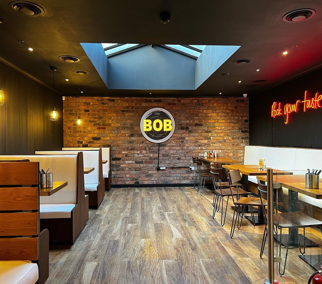 Modern interior of Band of Burgers Fulham with comfortable booths and a neon "BOB" sign.